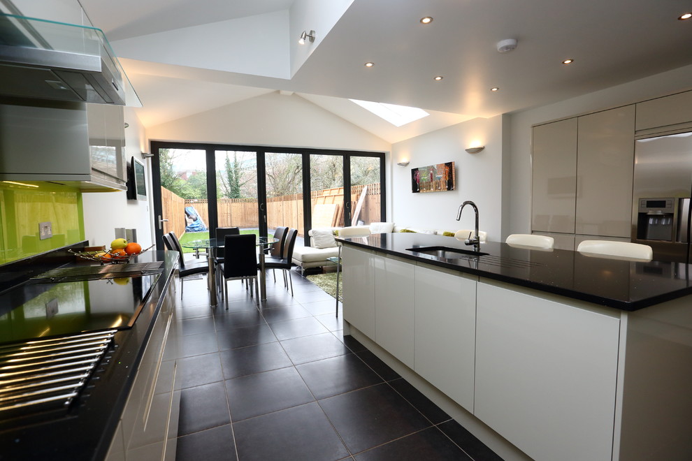 Large modern kitchen in London with an integrated sink, flat-panel cabinets, white cabinets, quartzite benchtops, yellow splashback, glass sheet splashback, white appliances, slate floors and with island.