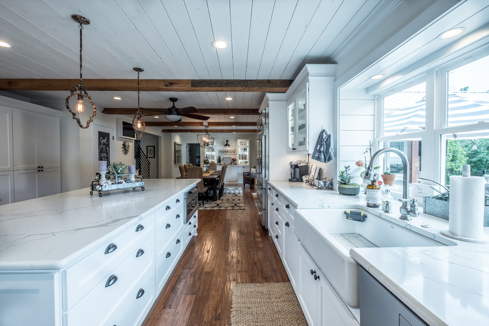 Inspiration for an expansive country eat-in kitchen in Charlotte with a farmhouse sink, white cabinets, quartz benchtops, white splashback, subway tile splashback, stainless steel appliances, light hardwood floors, with island, brown floor and white benchtop.
