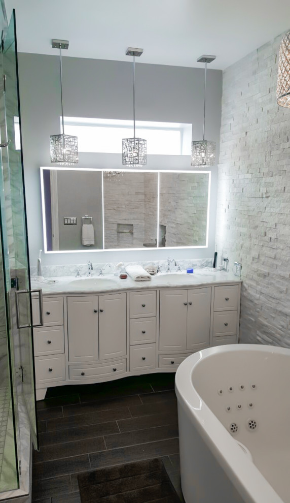 This is an example of a mid-sized traditional master bathroom in Los Angeles with raised-panel cabinets, white cabinets, a freestanding tub, a corner shower, a one-piece toilet, white tile, marble, white walls, porcelain floors, an undermount sink, marble benchtops, grey floor, a hinged shower door, white benchtops, a niche, a double vanity and a freestanding vanity.