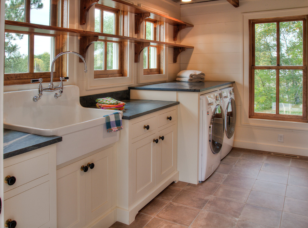 Design ideas for a mid-sized country single-wall dedicated laundry room in Minneapolis with a farmhouse sink, white cabinets, soapstone benchtops, white walls, ceramic floors, a side-by-side washer and dryer, beige floor and shaker cabinets.