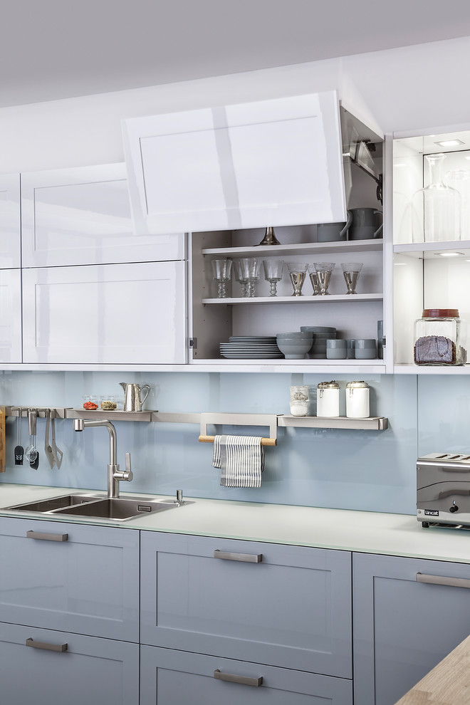 Inspiration for a contemporary kitchen in Stuttgart with a drop-in sink, shaker cabinets, grey splashback, glass sheet splashback, stainless steel appliances and blue cabinets.