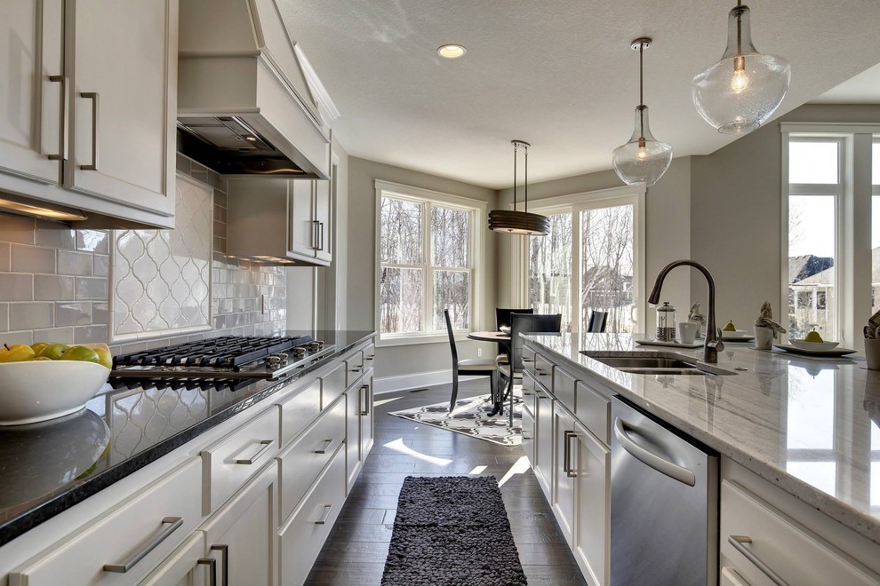 Mid-sized transitional l-shaped dark wood floor open concept kitchen photo in Minneapolis with a double-bowl sink, shaker cabinets, white cabinets, granite countertops, gray backsplash, subway tile backsplash, stainless steel appliances and an island