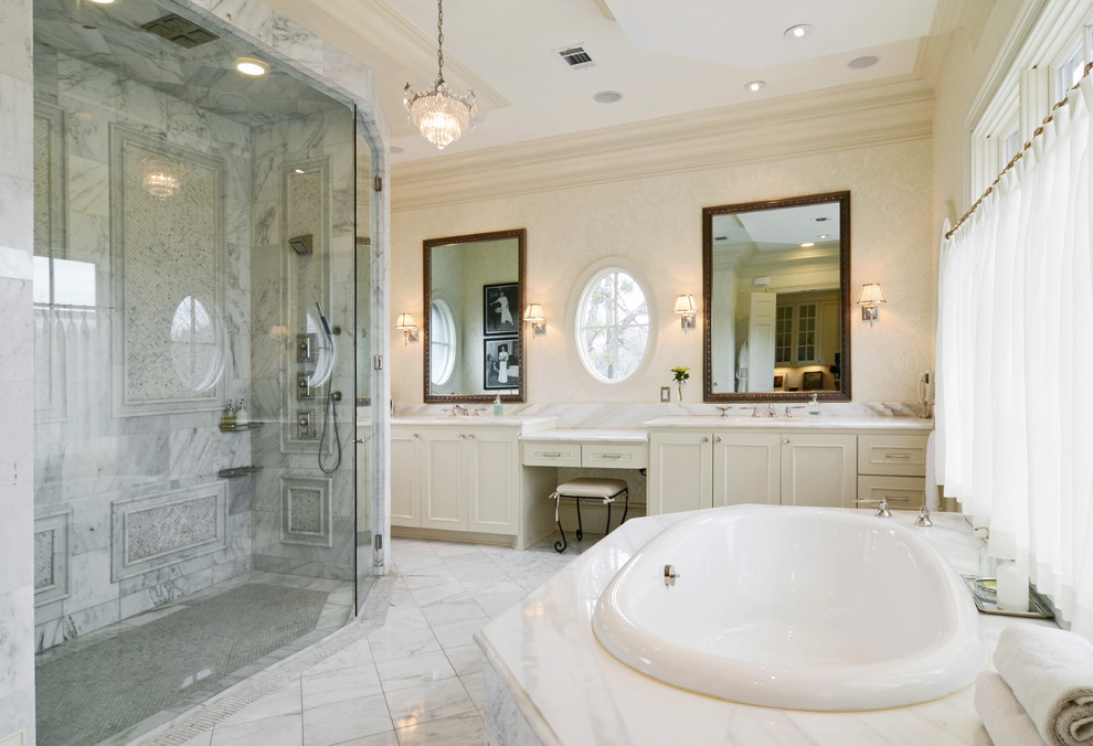 Photo of a large traditional master bathroom in Dallas with raised-panel cabinets, beige cabinets, a drop-in tub, an open shower, a one-piece toilet, beige walls, marble floors, an undermount sink, marble benchtops, white tile and stone tile.