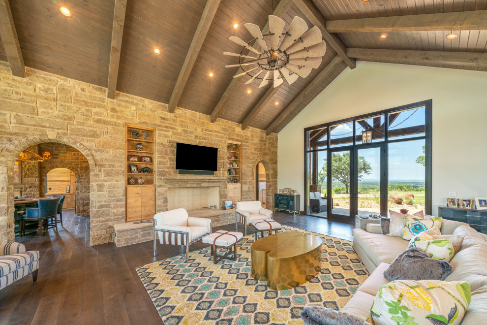 Design ideas for a large country open concept family room in Austin with beige walls, dark hardwood floors, a standard fireplace, a stone fireplace surround, a wall-mounted tv and brown floor.
