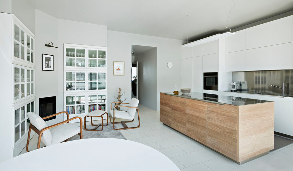 Inspiration for a mid-sized contemporary single-wall eat-in kitchen in Milan with flat-panel cabinets, white cabinets, stainless steel benchtops, metallic splashback, black appliances, with island and white floor.
