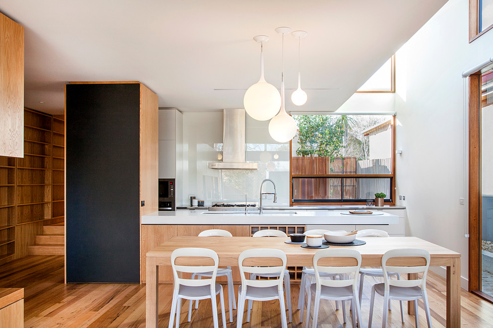 This is an example of a large contemporary galley eat-in kitchen in Melbourne with light wood cabinets, solid surface benchtops, white splashback, glass sheet splashback, stainless steel appliances, medium hardwood floors, with island, a double-bowl sink and shaker cabinets.