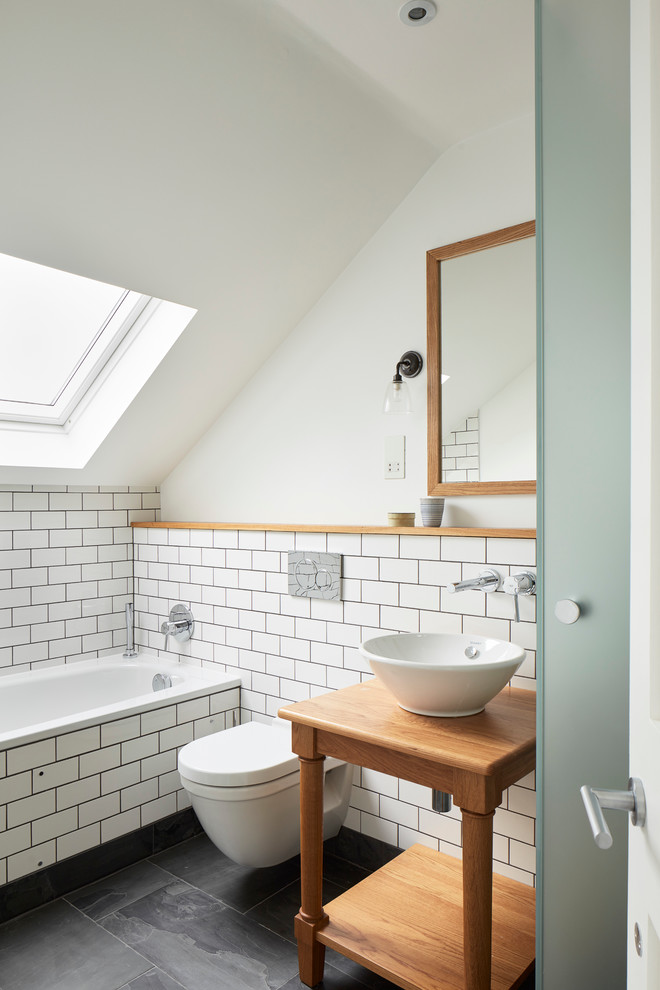 Small contemporary master bathroom in London with open cabinets, medium wood cabinets, a drop-in tub, a wall-mount toilet, white walls, slate floors, wood benchtops, a vessel sink, brown benchtops, a curbless shower, white tile, ceramic tile, grey floor, a hinged shower door, a single vanity and a built-in vanity.