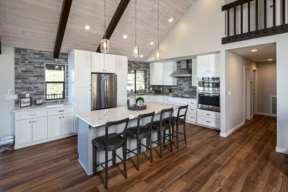 Transitional l-shaped dark wood floor, brown floor, exposed beam, vaulted ceiling and wood ceiling kitchen photo in Phoenix with a farmhouse sink, shaker cabinets, white cabinets, gray backsplash, stainless steel appliances, an island and white countertops
