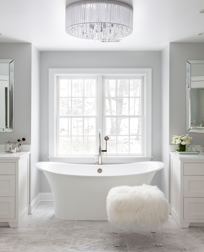 Inspiration for a large transitional master bathroom in New York with recessed-panel cabinets, white cabinets, a freestanding tub, an alcove shower, a one-piece toilet, white tile, marble, grey walls, marble floors, an undermount sink, recycled glass benchtops, grey floor and a hinged shower door.