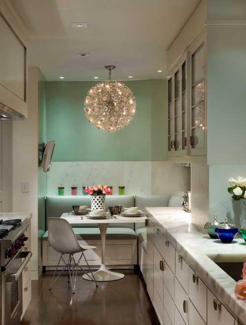 Light-colored shaker kitchen cabinets with glass-front uppers, mint accent wall, banquette nook, and under-cabinet lighting in a narrow kitchen