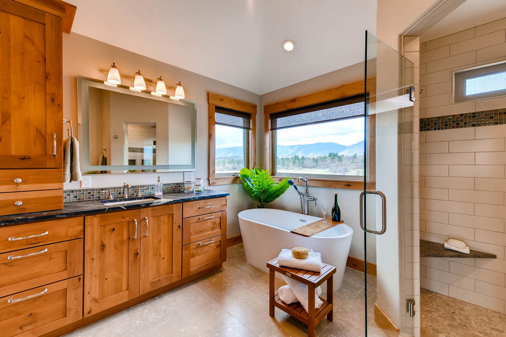 Design ideas for a large arts and crafts master bathroom in Denver with shaker cabinets, a freestanding tub, limestone floors, an undermount sink, soapstone benchtops, medium wood cabinets, beige walls, a hinged shower door, a corner shower, a two-piece toilet, beige tile, mosaic tile and grey floor.