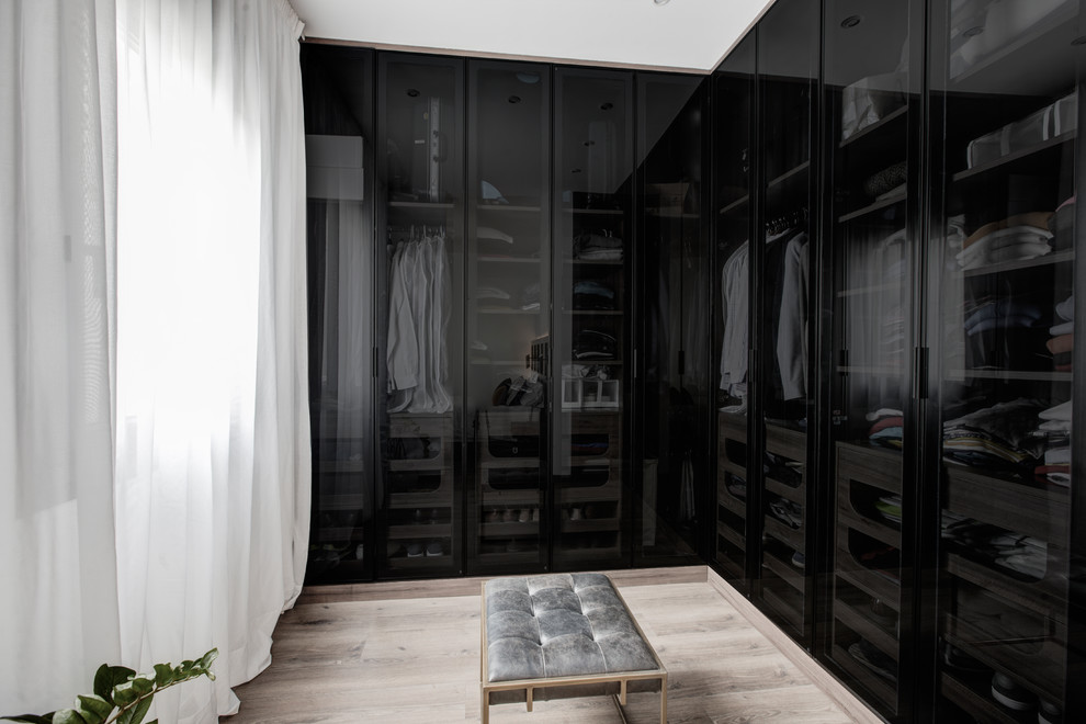 Photo of a mid-sized industrial men's dressing room in Madrid with glass-front cabinets, black cabinets, laminate floors and brown floor.