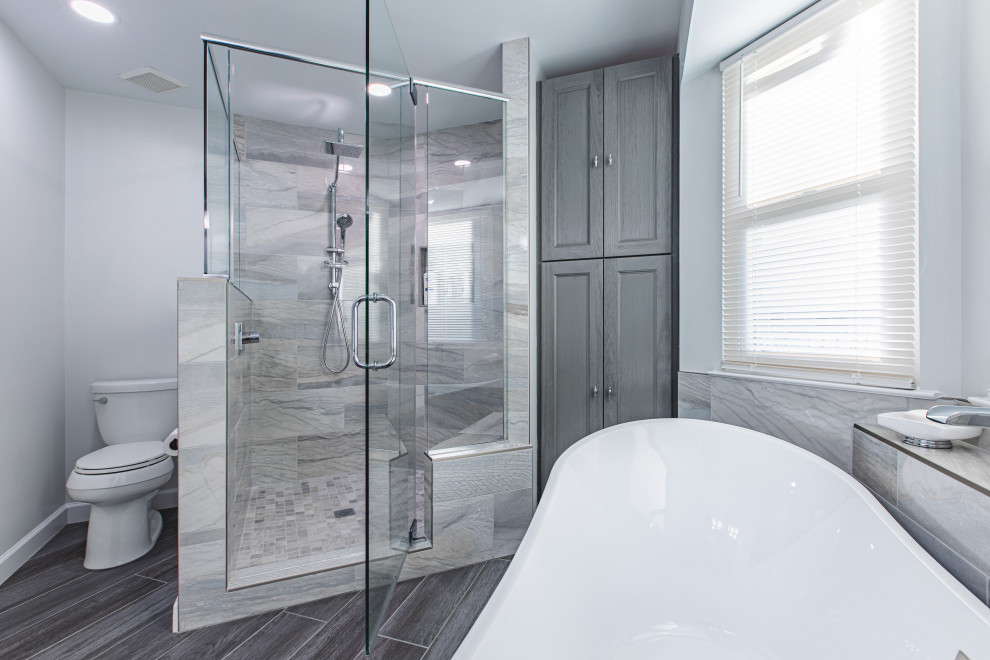 Large modern ensuite bathroom in Other with shaker cabinets, grey cabinets, a freestanding bath, a corner shower, a two-piece toilet, grey tiles, grey walls, porcelain flooring, a submerged sink, engineered stone worktops, brown floors, a hinged door, double sinks and a built in vanity unit.