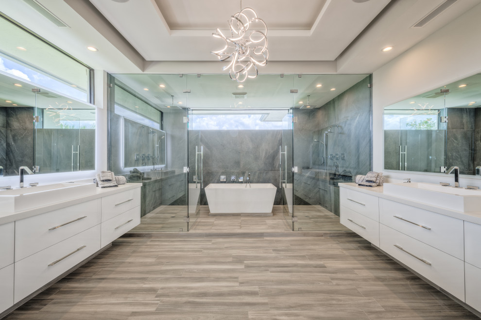Inspiration for a large transitional master wet room bathroom in Miami with a freestanding tub, gray tile, marble, beige walls, terra-cotta floors, engineered quartz benchtops, brown floor, a hinged shower door and white benchtops.