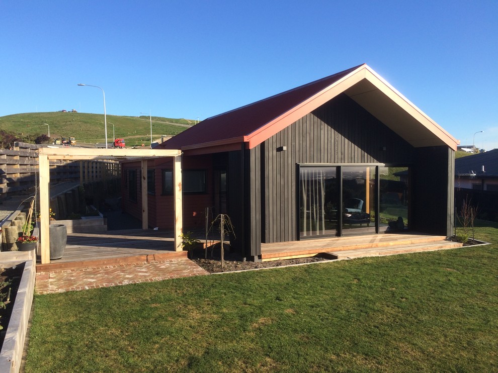Small country one-storey black house exterior in Christchurch with wood siding, a gable roof and a metal roof.
