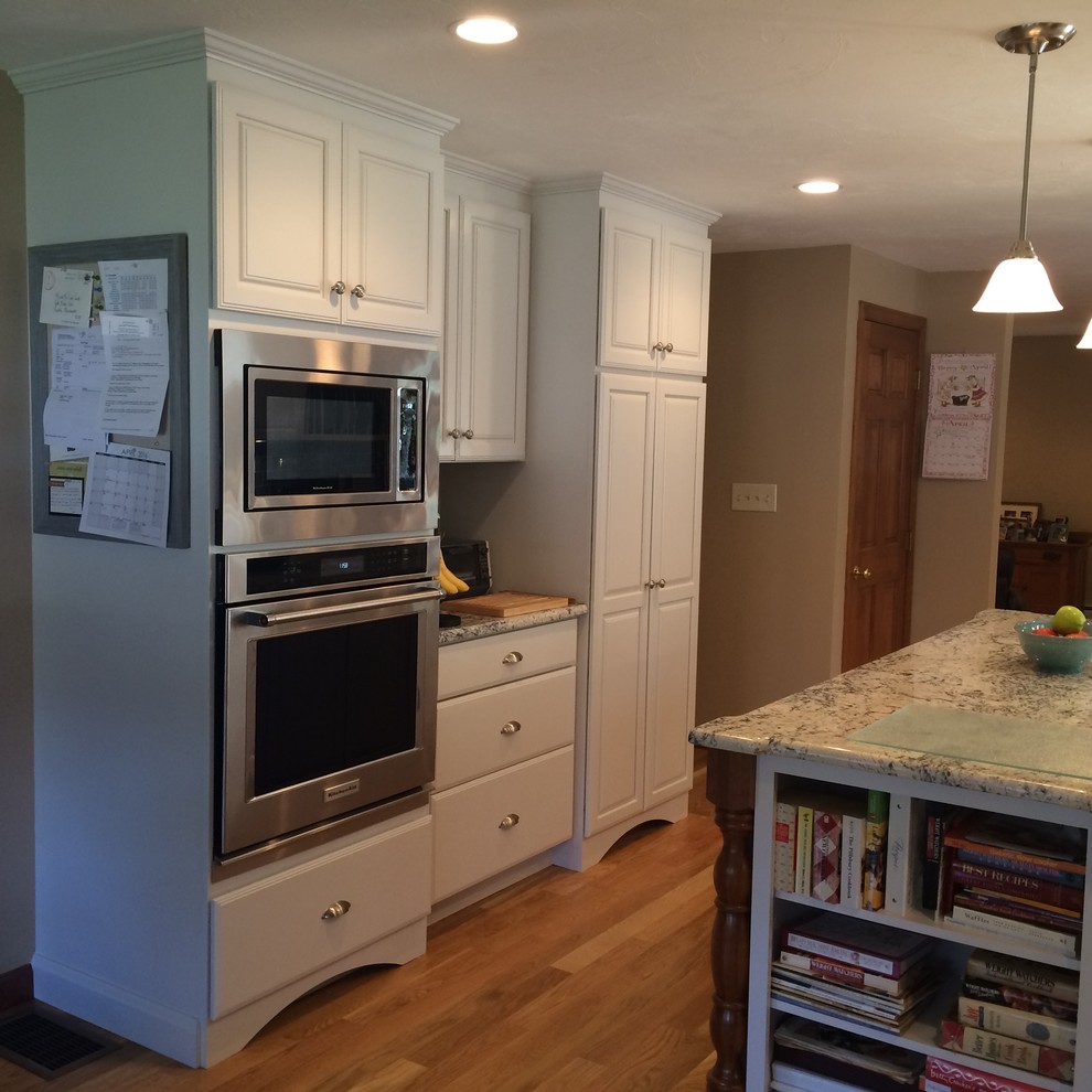 Example of a transitional u-shaped medium tone wood floor eat-in kitchen design in Boston with an undermount sink, raised-panel cabinets, white cabinets, granite countertops, blue backsplash, glass tile backsplash, stainless steel appliances and an island