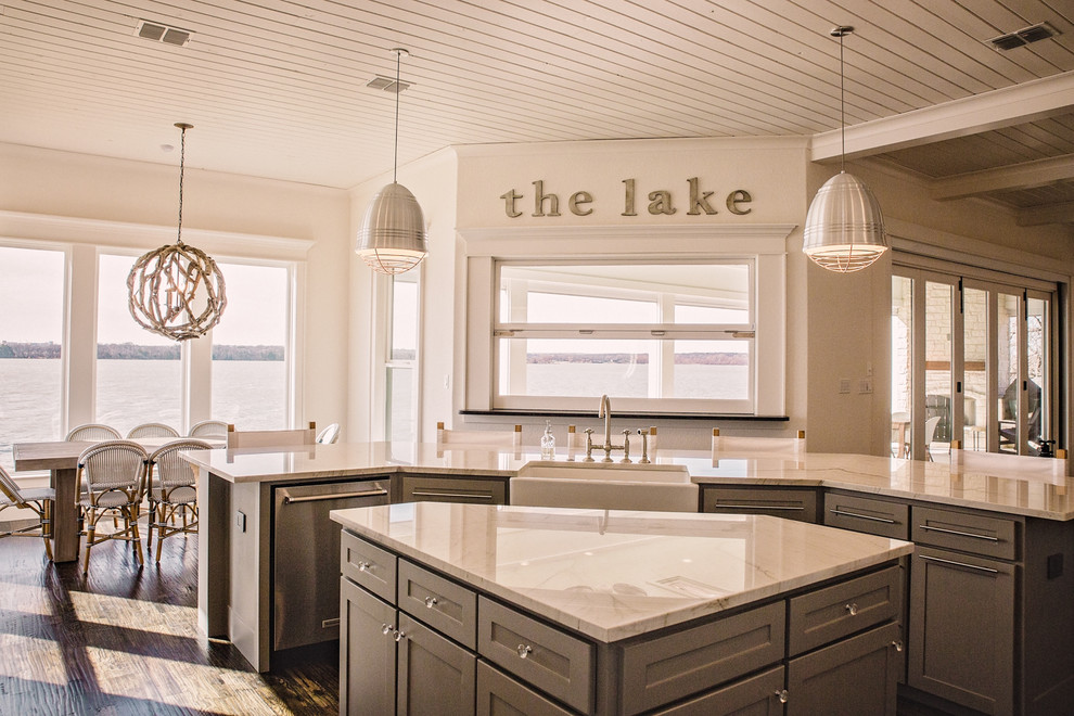 Large beach style l-shaped open plan kitchen in Dallas with a farmhouse sink, shaker cabinets, white cabinets, marble benchtops, white splashback, ceramic splashback, stainless steel appliances, dark hardwood floors, multiple islands and brown floor.
