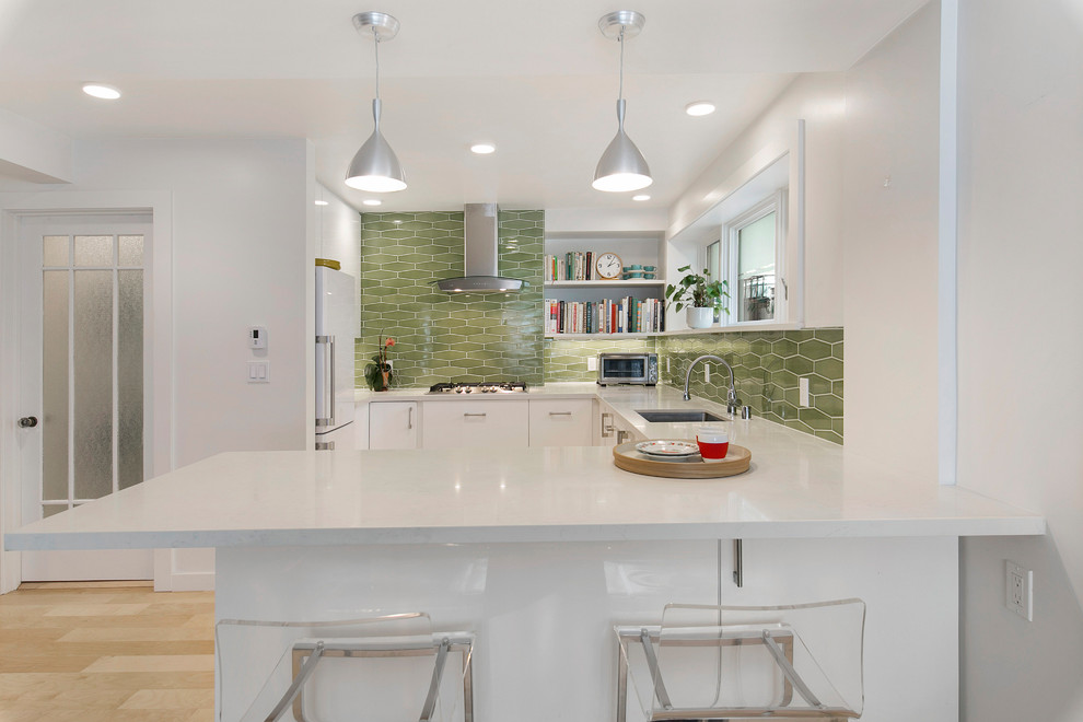 Design ideas for a contemporary u-shaped kitchen in San Francisco with an undermount sink, flat-panel cabinets, white cabinets, green splashback, white appliances, light hardwood floors, a peninsula, beige floor and white benchtop.