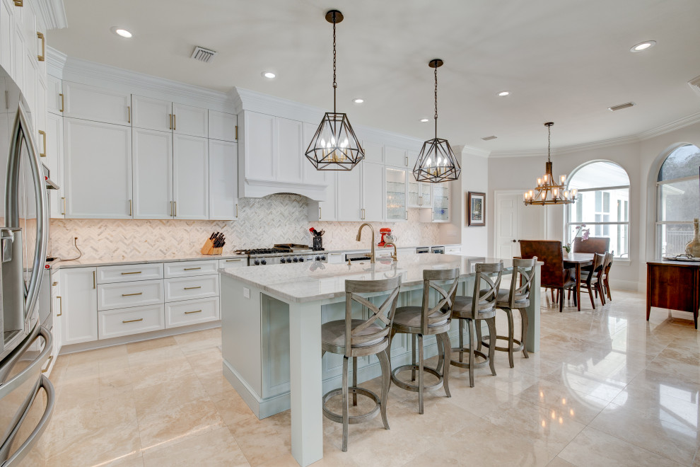 This is an example of a classic l-shaped kitchen/diner in Miami with a submerged sink, white cabinets, engineered stone countertops, multi-coloured splashback, marble splashback, stainless steel appliances, travertine flooring, an island, beige floors and white worktops.