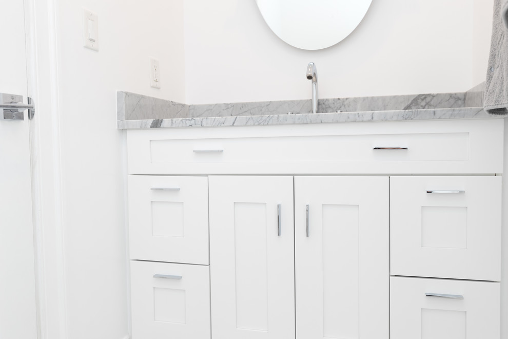 Inspiration for a mid-sized contemporary powder room in DC Metro with white cabinets, a two-piece toilet, white tile, subway tile, white walls, ceramic floors, an undermount sink, solid surface benchtops and white floor.