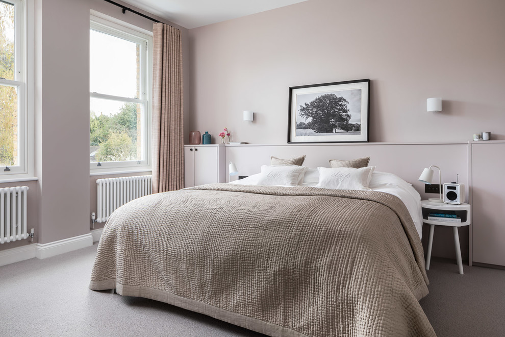 Contemporary master bedroom in London with pink walls, carpet, no fireplace and grey floor.