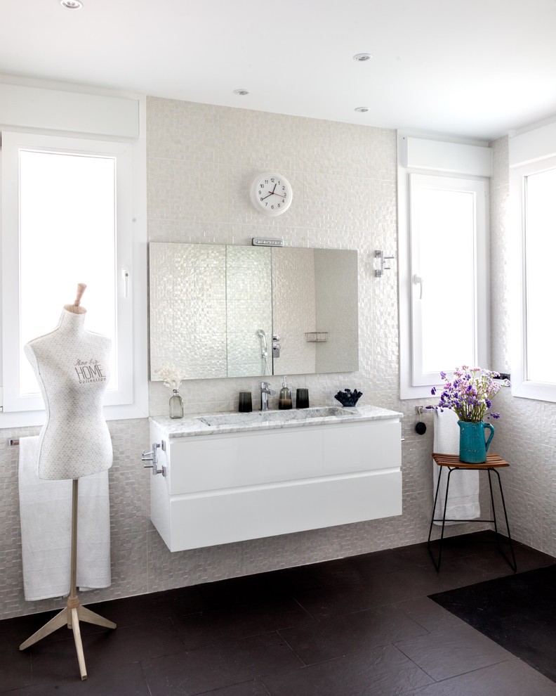 This is an example of a mid-sized modern master bathroom in Madrid with flat-panel cabinets, white cabinets, a curbless shower, a one-piece toilet, white tile, ceramic tile, white walls, slate floors, a trough sink, marble benchtops and black floor.