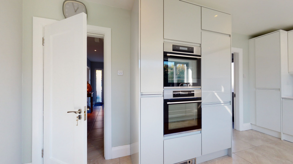 Inspiration for a mid-sized modern u-shaped kitchen in Other with an integrated sink, glass-front cabinets, white cabinets, solid surface benchtops, white splashback, panelled appliances, porcelain floors, a peninsula, beige floor and white benchtop.