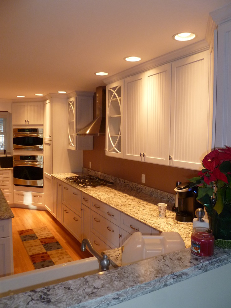 Inspiration for a large traditional u-shaped kitchen in Boston with a farmhouse sink, white cabinets, granite benchtops, stainless steel appliances, light hardwood floors and with island.