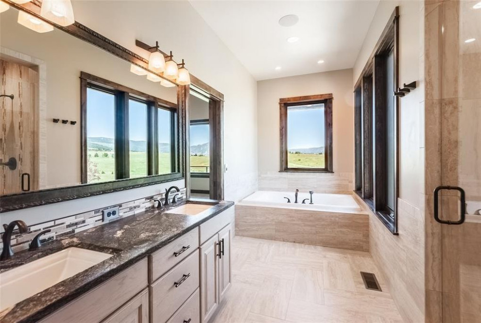 Large transitional master beige tile and slate tile slate floor, beige floor and double-sink drop-in bathtub photo with recessed-panel cabinets, beige cabinets, beige walls, an undermount sink, a hinged shower door, black countertops and a built-in vanity
