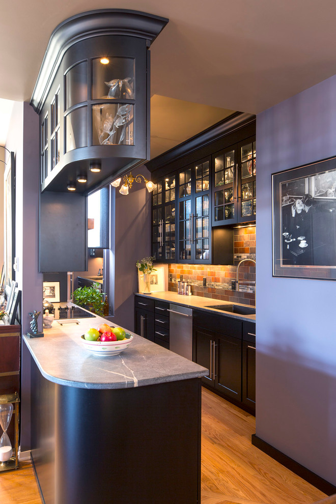 Inspiration for a small transitional galley medium tone wood floor enclosed kitchen remodel in Minneapolis with an undermount sink, shaker cabinets, black cabinets, soapstone countertops, porcelain backsplash, stainless steel appliances and a peninsula