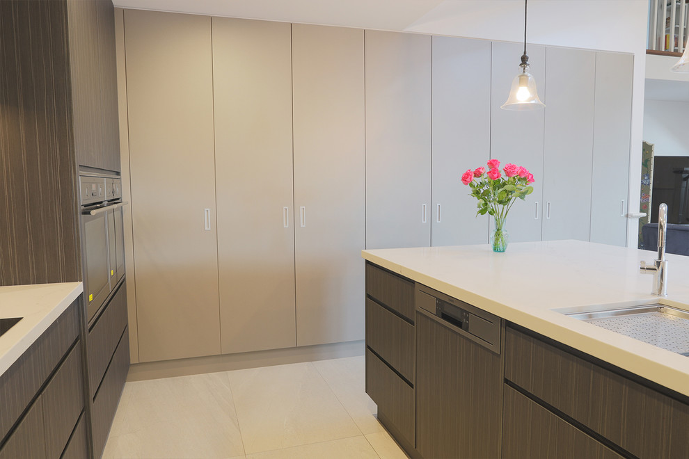 This is an example of an expansive modern galley open plan kitchen in Central Coast with an undermount sink, flat-panel cabinets, dark wood cabinets, quartz benchtops, white splashback, stone slab splashback, stainless steel appliances, porcelain floors, with island, white floor and white benchtop.