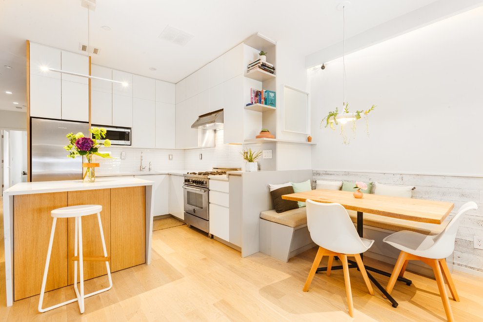 Small modern l-shaped open plan kitchen in New York with an undermount sink, flat-panel cabinets, white cabinets, quartzite benchtops, white splashback, stainless steel appliances, light hardwood floors, with island and beige floor.