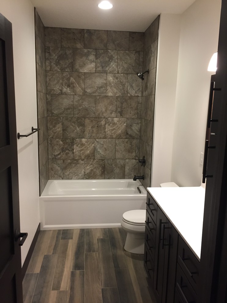 Small arts and crafts kids bathroom in Cedar Rapids with shaker cabinets, dark wood cabinets, an alcove tub, a shower/bathtub combo, a two-piece toilet, gray tile, beige walls, laminate floors, an undermount sink, a shower curtain and brown floor.