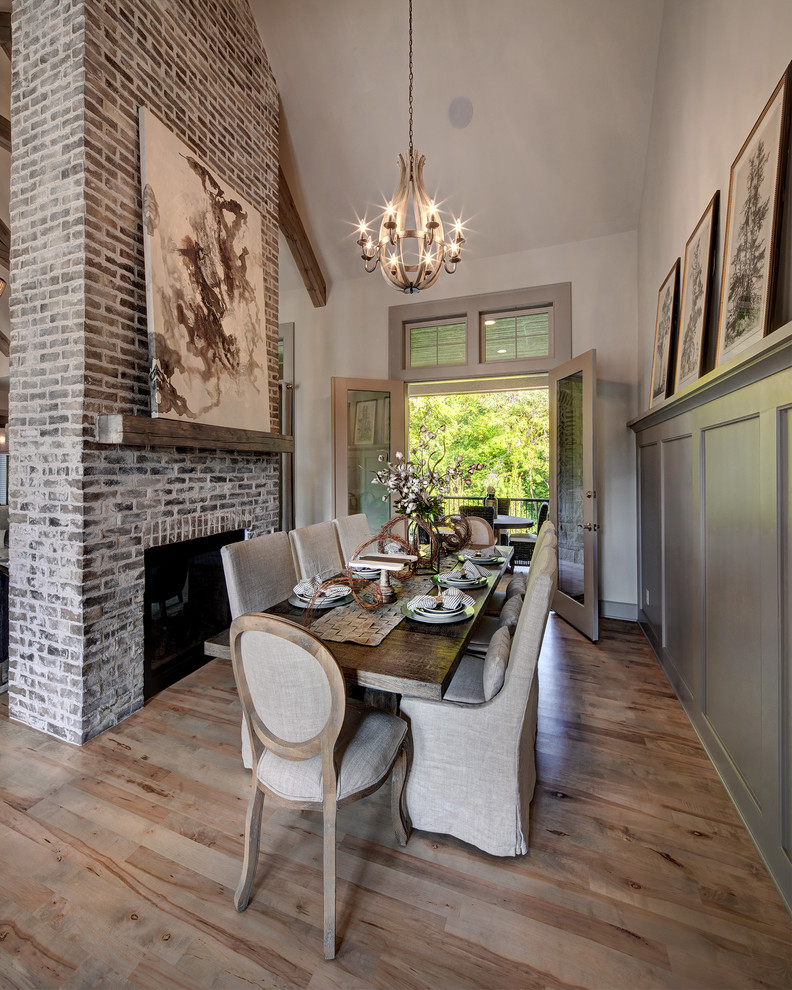 Photo of a country dining room in Kansas City with beige walls, light hardwood floors, a standard fireplace, a brick fireplace surround and beige floor.