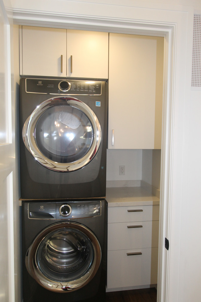 Design ideas for a small transitional laundry cupboard in San Francisco with flat-panel cabinets, white cabinets, quartz benchtops, engineered quartz splashback, dark hardwood floors, a stacked washer and dryer, brown floor and white benchtop.