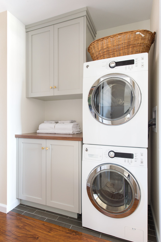 This is an example of a small midcentury laundry room in San Diego with shaker cabinets, quartz benchtops, white walls, limestone floors, a stacked washer and dryer, black floor and grey cabinets.