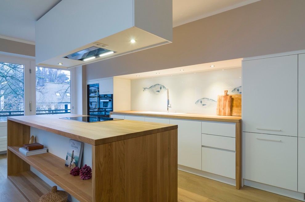 Design ideas for a large contemporary kitchen in Hamburg with white cabinets, wood benchtops, white splashback, glass sheet splashback, medium hardwood floors and with island.