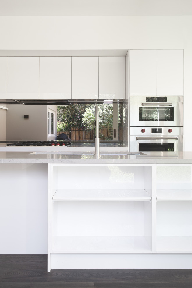 Mid-sized modern single-wall separate kitchen in Sydney with an undermount sink, flat-panel cabinets, white cabinets, marble benchtops, mirror splashback, stainless steel appliances, dark hardwood floors, with island, brown floor and white benchtop.