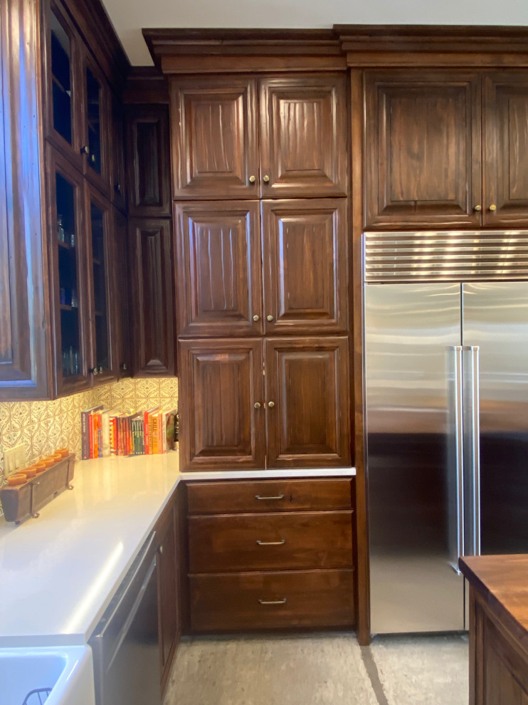 Mid-sized mountain style u-shaped concrete floor and gray floor eat-in kitchen photo in Phoenix with a farmhouse sink, raised-panel cabinets, distressed cabinets, wood countertops, multicolored backsplash, ceramic backsplash, stainless steel appliances, an island and brown countertops