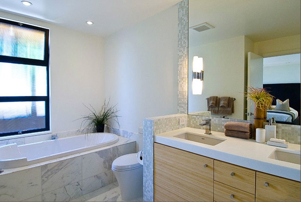 Inspiration for a contemporary master bathroom in San Francisco with an undermount sink, flat-panel cabinets, light wood cabinets, a drop-in tub, a two-piece toilet, blue tile, glass tile, white walls and marble floors.