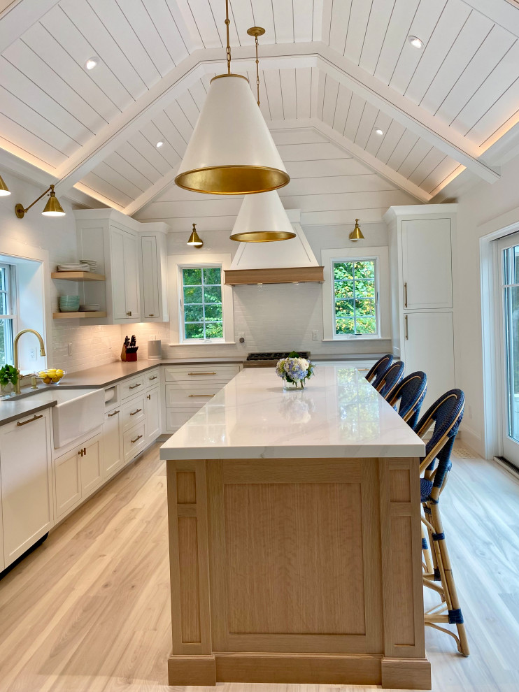 This is an example of a beach style kitchen in Boston with a farmhouse sink, shaker cabinets, white cabinets, quartz benchtops, white splashback, ceramic splashback, panelled appliances, medium hardwood floors, with island, white benchtop and vaulted.