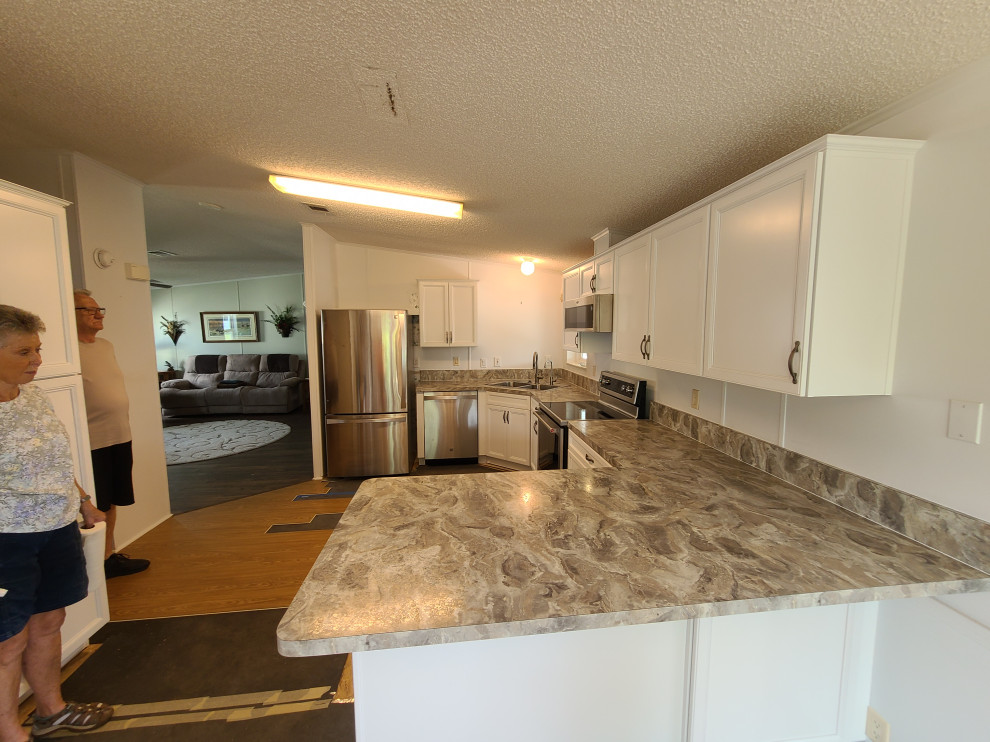 Example of a large l-shaped eat-in kitchen design with a double-bowl sink, flat-panel cabinets, white cabinets, laminate countertops, stainless steel appliances, a peninsula and white countertops