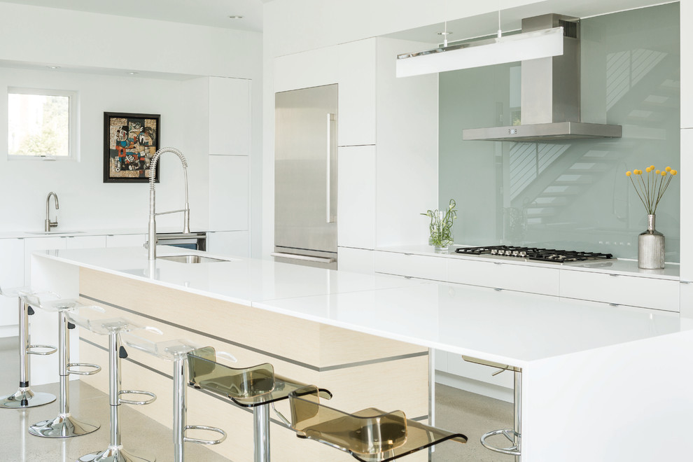 Design ideas for a large modern galley open plan kitchen in Portland Maine with an undermount sink, flat-panel cabinets, white cabinets, quartz benchtops, glass sheet splashback, stainless steel appliances, with island, grey splashback and concrete floors.