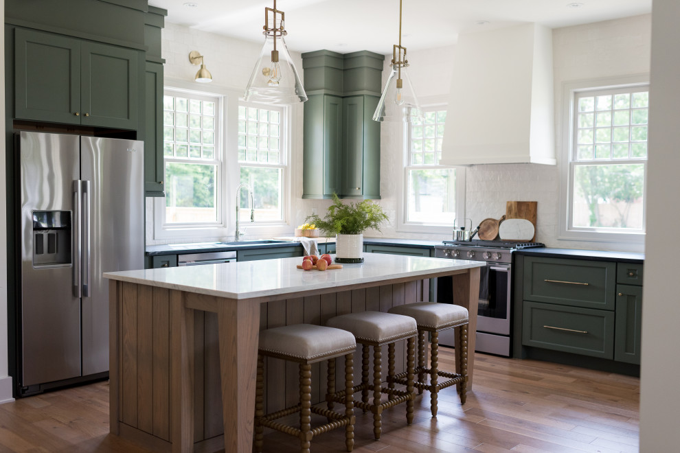 Transitional medium tone wood floor and brown floor kitchen photo in Indianapolis with an undermount sink, shaker cabinets, green cabinets, white backsplash, stainless steel appliances, an island and black countertops