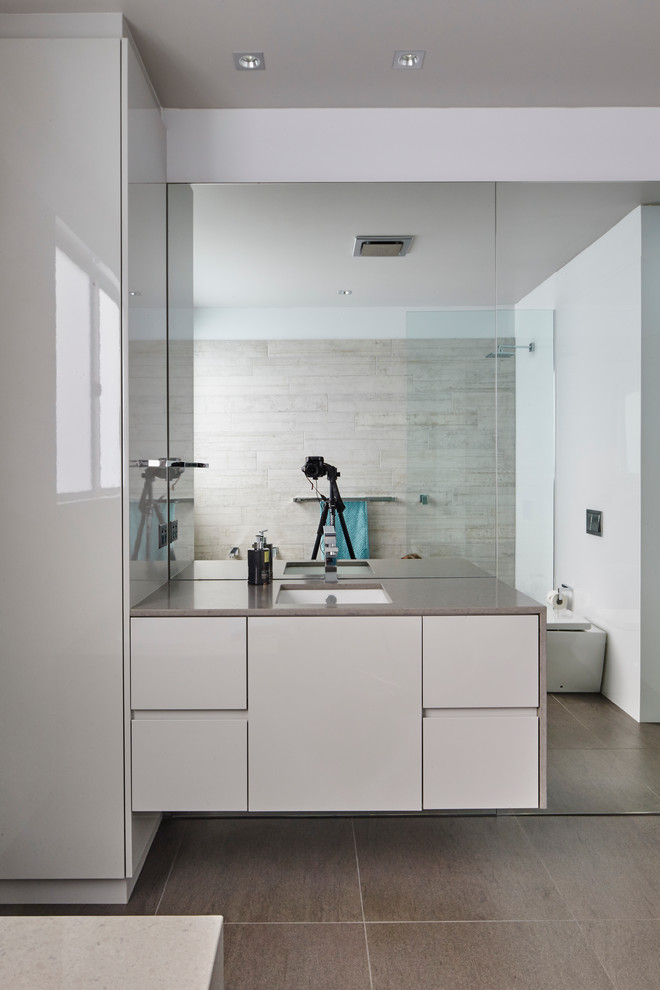 Mid-sized modern master bathroom in Wollongong with grey cabinets, an undermount tub, an open shower, a one-piece toilet, gray tile, ceramic floors and engineered quartz benchtops.