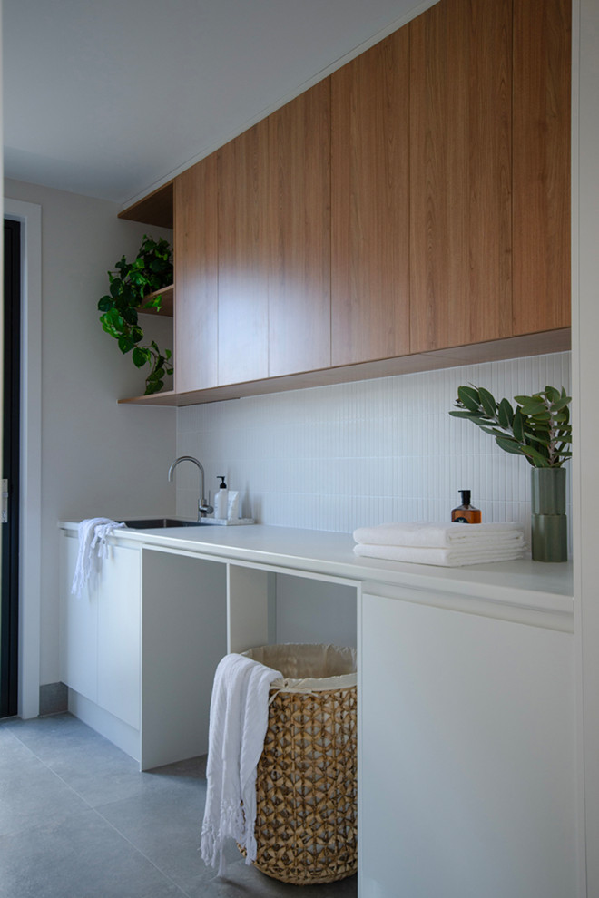 Modern single-wall dedicated laundry room in Canberra - Queanbeyan with laminate benchtops, white splashback, mosaic tile splashback, porcelain floors, grey floor and white benchtop.