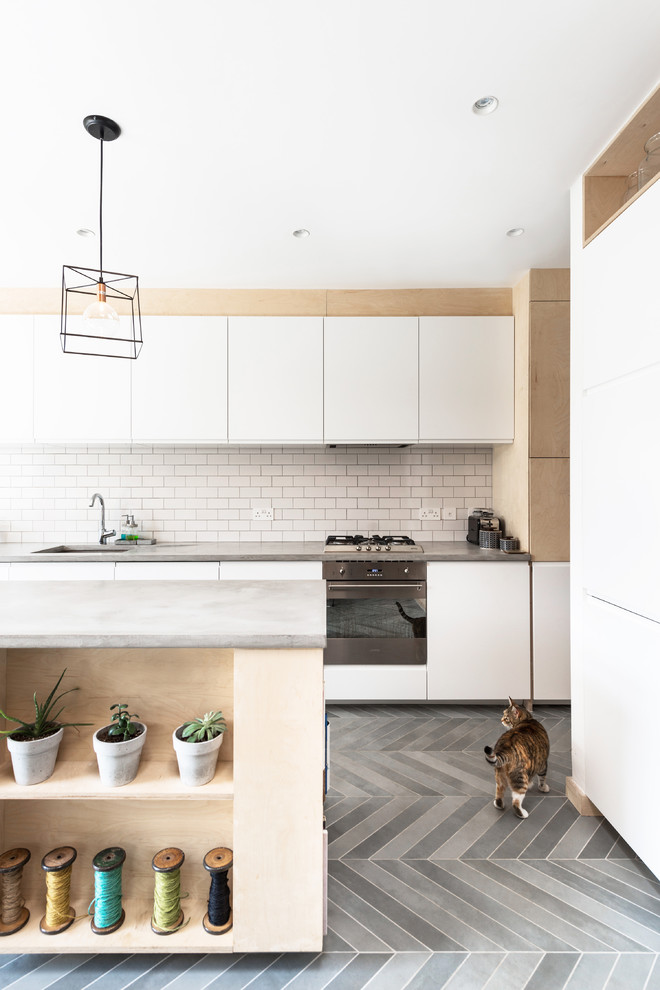 Scandinavian kitchen in London with a single-bowl sink, flat-panel cabinets, white cabinets, concrete benchtops, white splashback, subway tile splashback, with island, grey floor and grey benchtop.