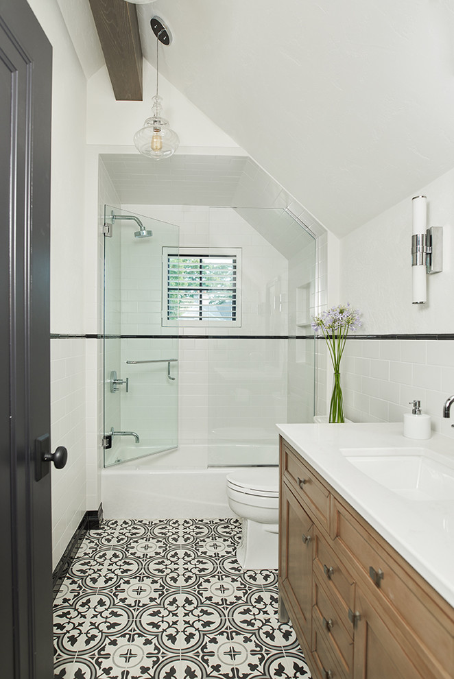 Transitional bathroom in Grand Rapids with brown cabinets, a drop-in tub, a shower/bathtub combo, a two-piece toilet, white tile, subway tile, white walls, an undermount sink, multi-coloured floor, a hinged shower door, white benchtops, a single vanity, a freestanding vanity and exposed beam.