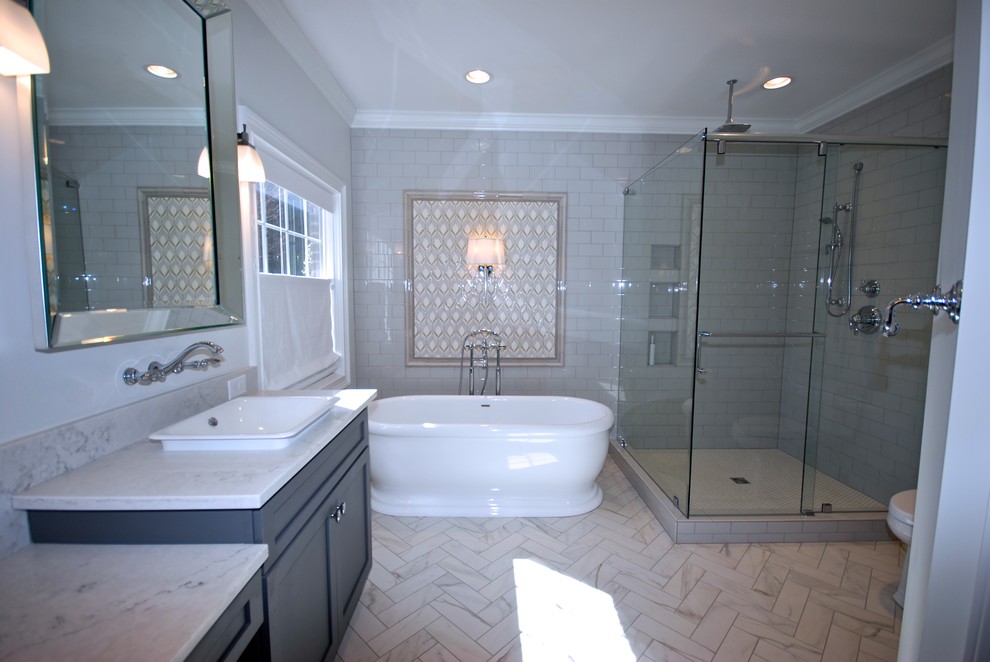 Inspiration for a mid-sized transitional master bathroom in Other with grey cabinets, a freestanding tub, a corner shower, a two-piece toilet, porcelain tile, grey walls, porcelain floors, recessed-panel cabinets, gray tile, a drop-in sink, marble benchtops and a hinged shower door.