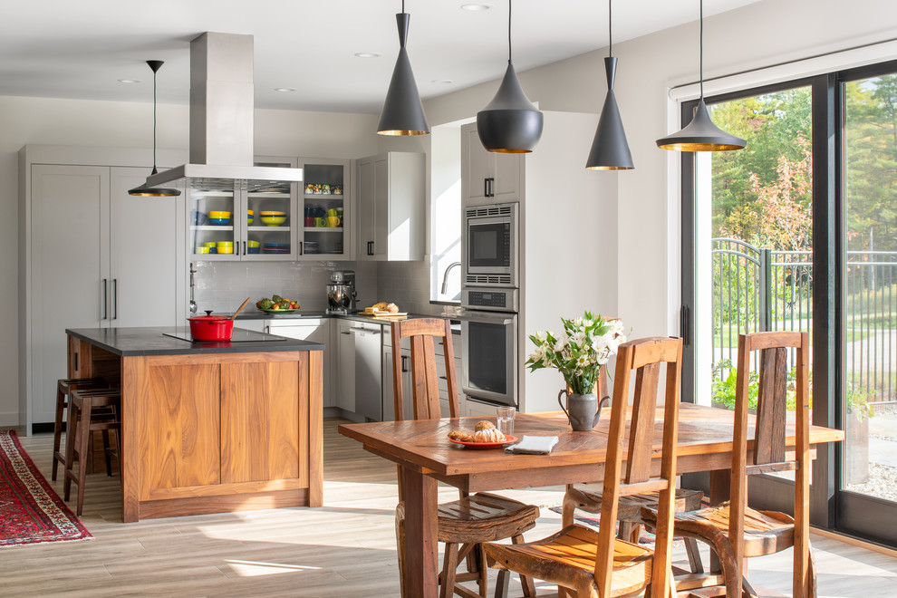 Design ideas for a mid-sized country l-shaped eat-in kitchen in Burlington with an undermount sink, shaker cabinets, grey cabinets, soapstone benchtops, white splashback, subway tile splashback, stainless steel appliances, porcelain floors, with island, beige floor and black benchtop.